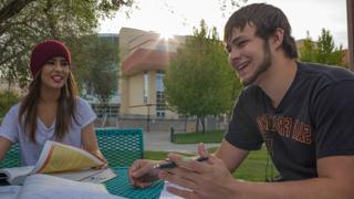 Image of two students sitting at a table outside talking.